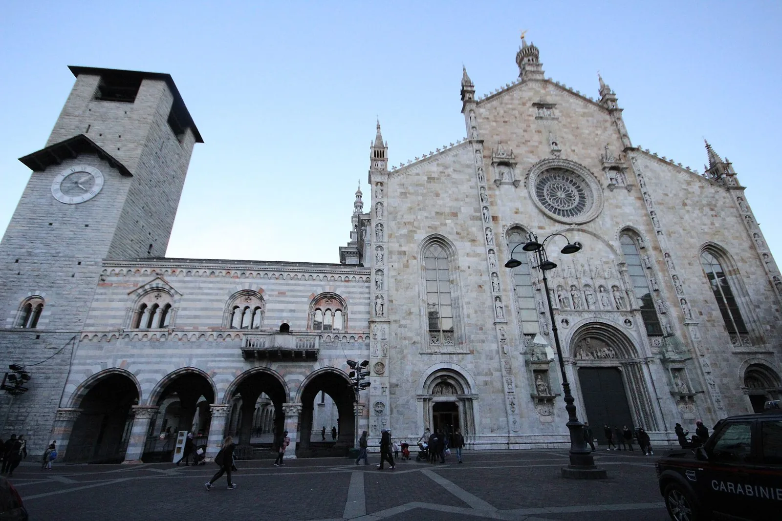 La facciata gotica in marmo del Duomo di Como con a sinistra il Broletto a fasce colorate e la torre civica con l'orologio, in piazza del Duomo