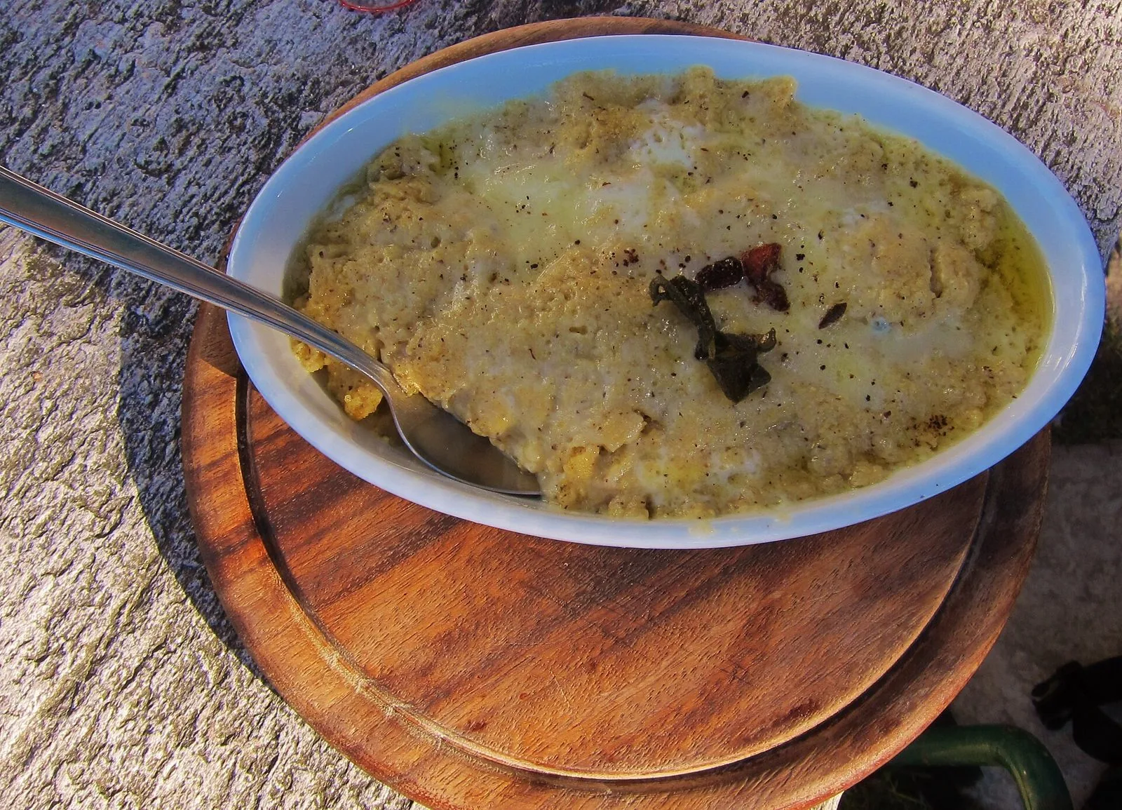 Pirofila di polenta uncia con formaggio fuso, burro e foglie di salvia fritte, servita su un tagliere di legno
