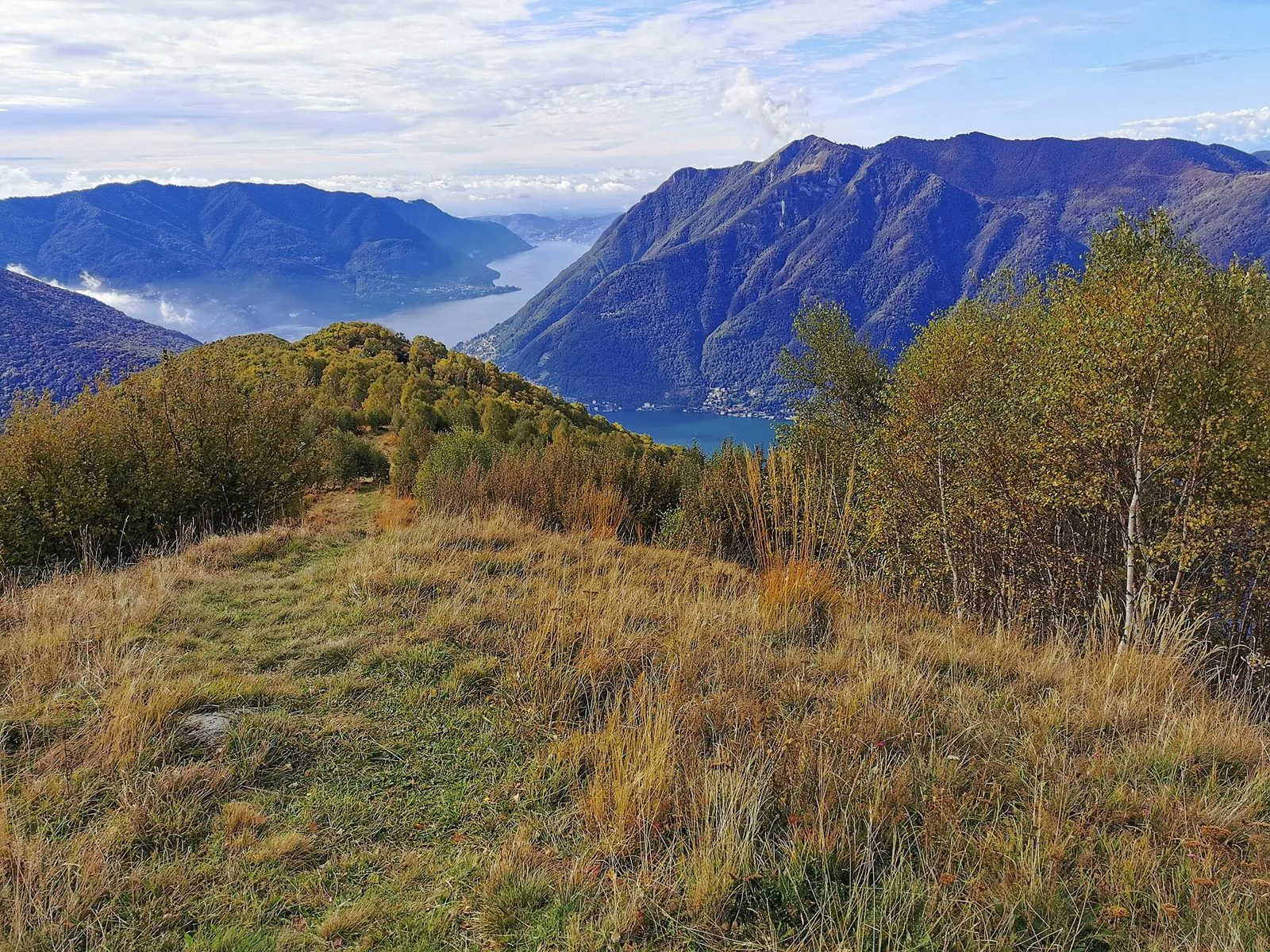 Il lago di Como visto dall'alto da un sentiero sopra Veleso, tra prati autunnali e montagne che scendono a picco sull'acqua