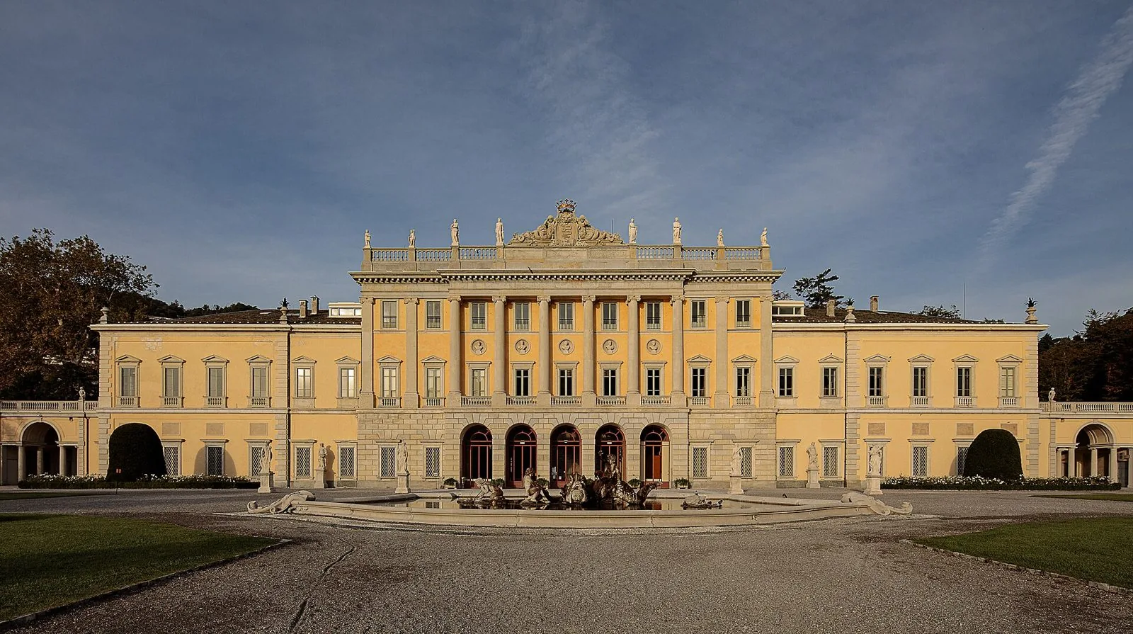 La facciata neoclassica gialla di Villa Olmo a Como con colonne, statue sul coronamento e la fontana nel giardino antistante